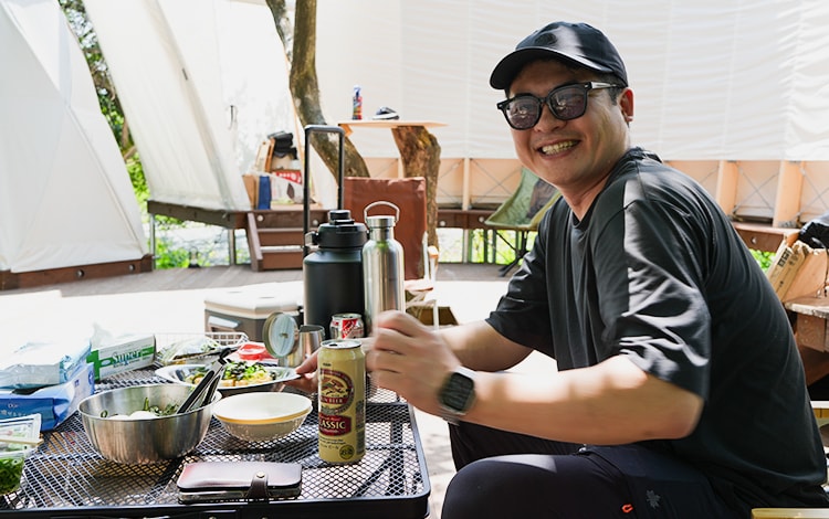 キャンプ場で料理とビールを楽しむ男性